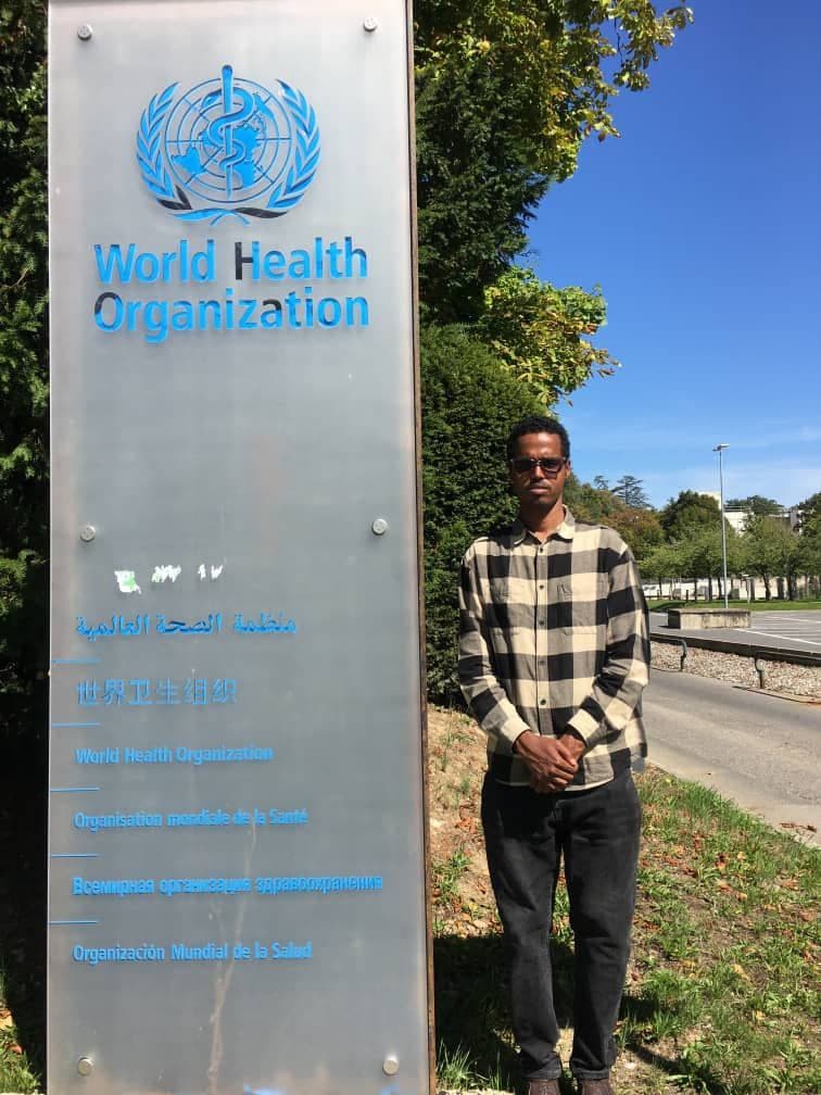 SHIFA's Founder standing beside the World Health Organization headquarters sign in Geneva, Switzerland